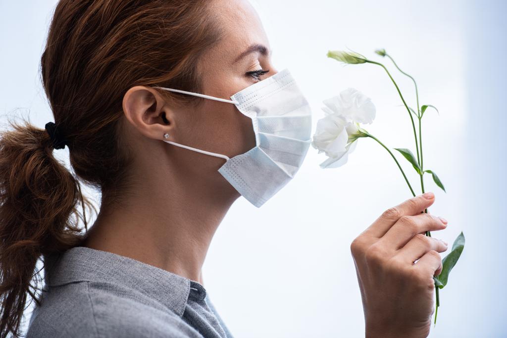 Seitenansicht einer Frau in medizinischer Maske, die Blumen riecht  - Foto, Bild
