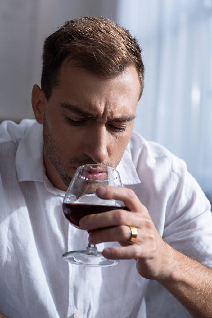 depressieve man in shirt drinken Cognac thuis - Foto, afbeelding