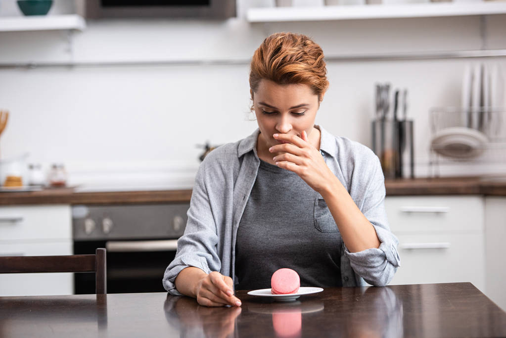 attraktive Frau, die den Mund bedeckt, während sie leckeres Dessert betrachtet  - Foto, Bild