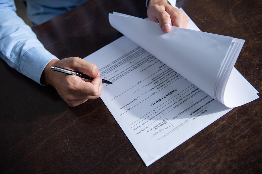 Teilansicht eines Mannes, der am Tisch sitzt und Scheidungsurkunden unterzeichnet - Foto, Bild