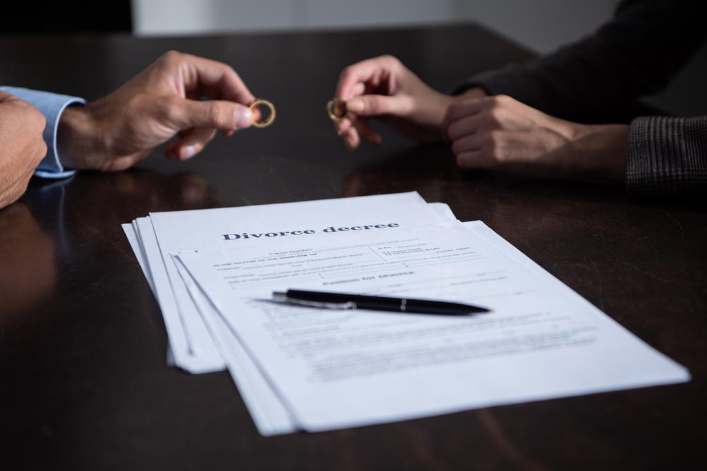 partial view of couple at table with divorce documents holding rings - Photo, Image