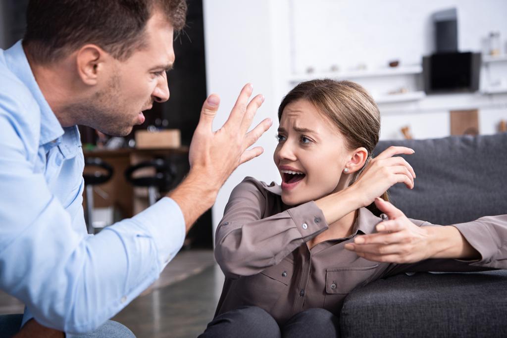 agresivo hombre en camisa gritando a asustado esposa en casa
 - Foto, Imagen