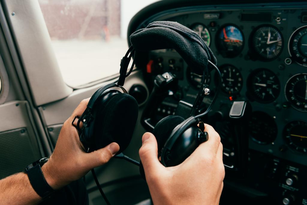vista parziale del pilota in orologio da polso che tiene le cuffie in aereo
 - Foto, immagini