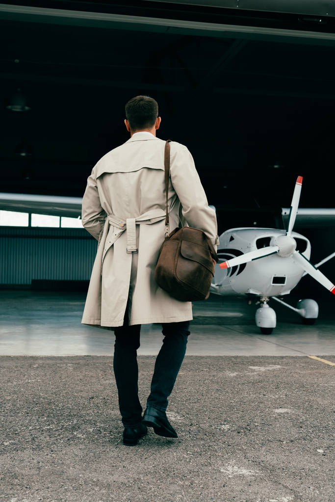 飛行機の近くに立っているコートでスタイリッシュなビジネスマンのバックビュー - 写真・画像