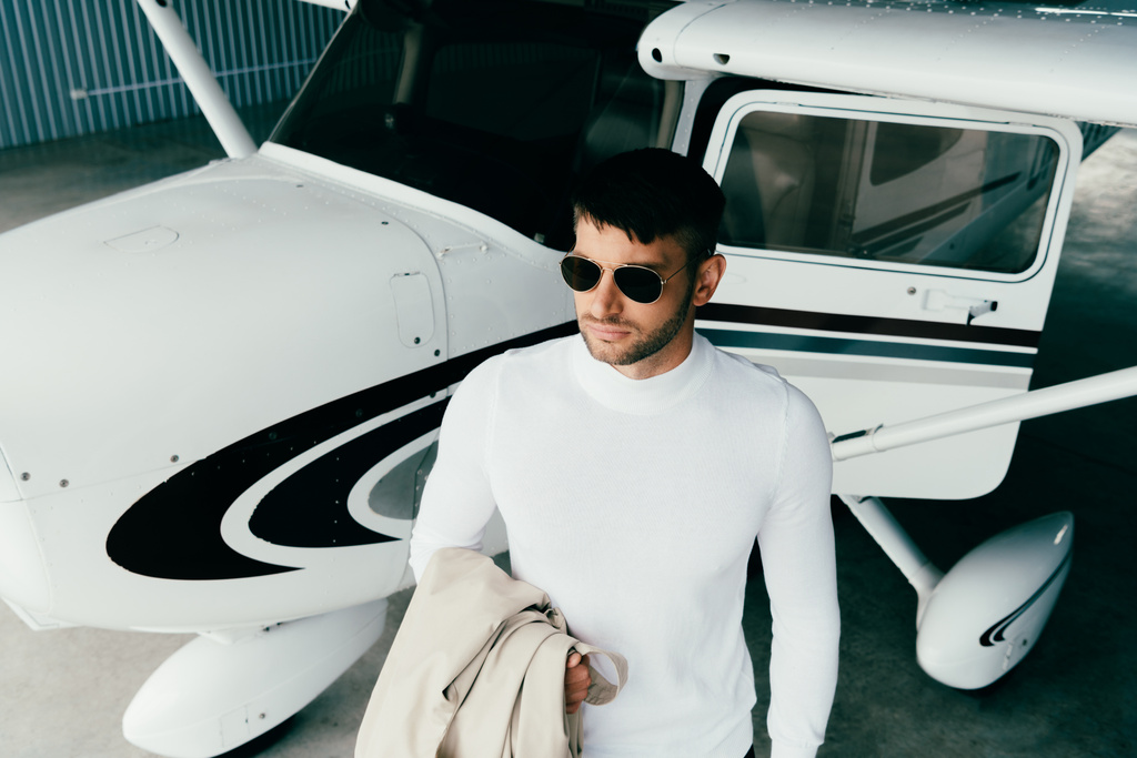 high angle view of man in sunglasses and casual attire standing near plane and looking away - Photo, Image
