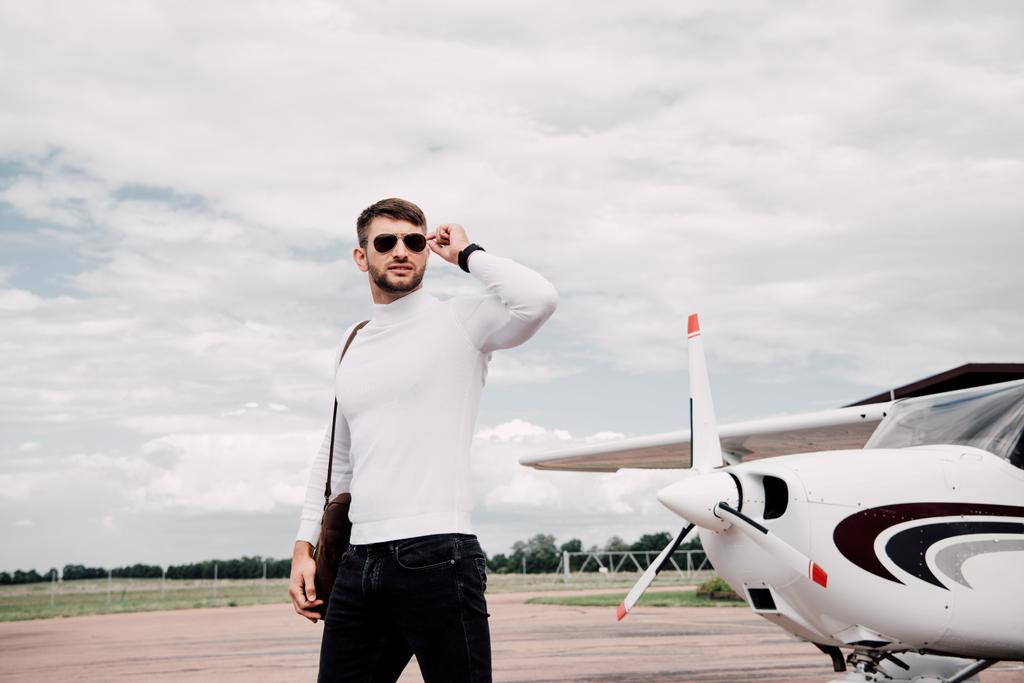 曇り空の下で飛行機の近くに立っているバッグを持つサングラスをかけた男 ロイヤリティフリー写真 画像素材