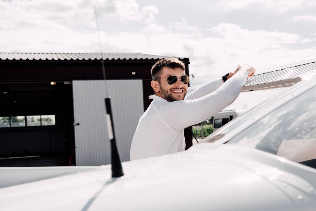χαμογελαστός άντρας με γυαλιά ηλίου να στέκεται κοντά στο αεροπλάνο την ηλιόλουστη μέρα - Φωτογραφία, εικόνα