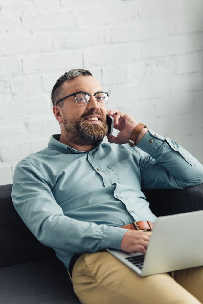 bel homme d'affaires en chemise tenant ordinateur portable et parlant sur smartphone au bureau
  - Photo, image