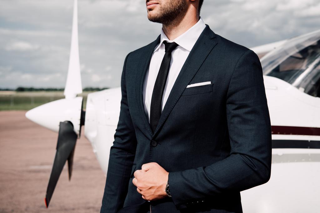 飛行機の近くに立っているフォーマルな服を着たひげを生やしたビジネスマンの部分的なビュー - 写真・画像