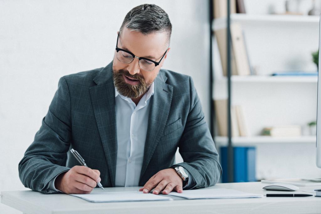 handsome businessman in formal wear and glasses writing with pen in office  - Photo, Image