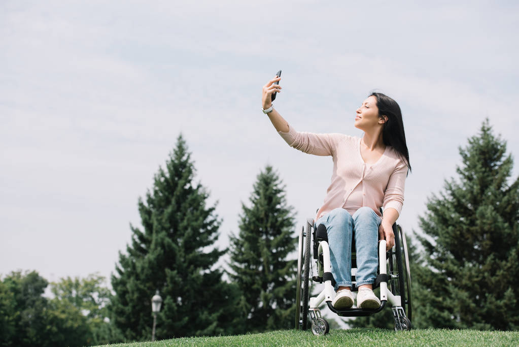 公園を歩きながらスマートフォンで自分撮りをする幸せな障害のある女性 - 写真・画像