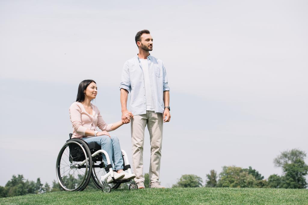 bonito jovem homem de mãos dadas com deficiência namorada sentado em cadeira de rodas
 - Foto, Imagem