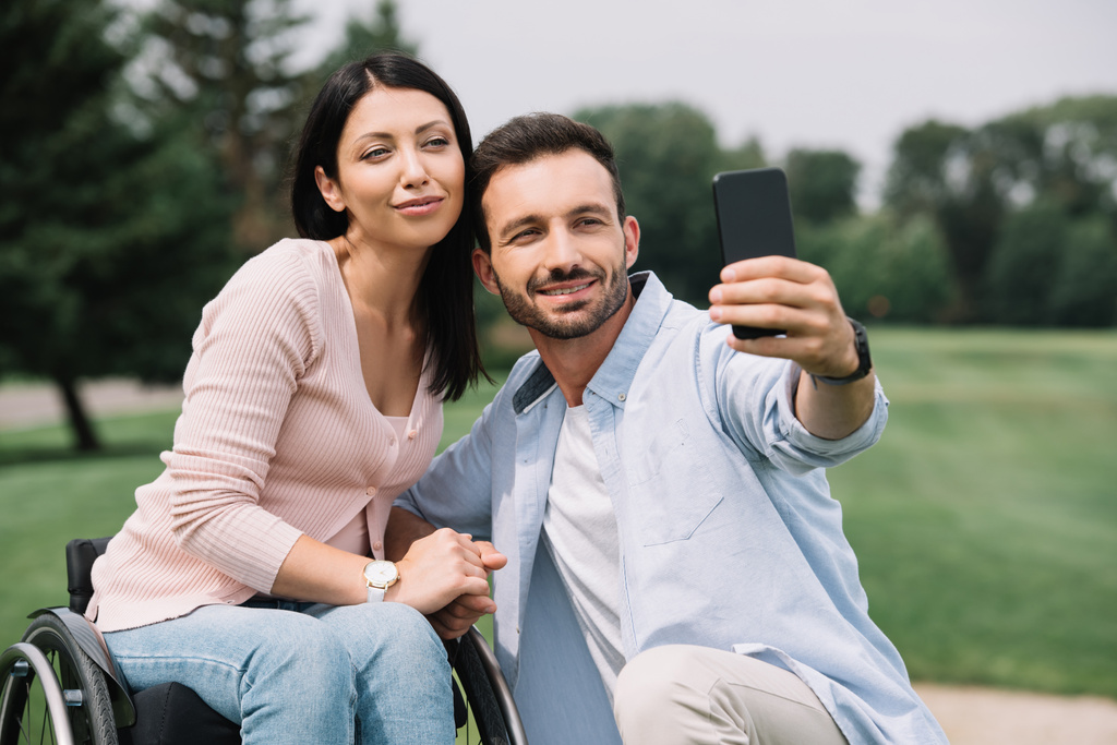 χαρούμενος άνθρωπος παίρνοντας selfie στο smartphone με χαμογελαστή κοπέλα με αναπηρία στο πάρκο - Φωτογραφία, εικόνα