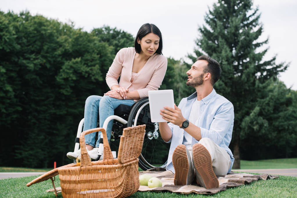 cheerful disabled woman and smiling boyfriend using digital tablet in park - Photo, Image