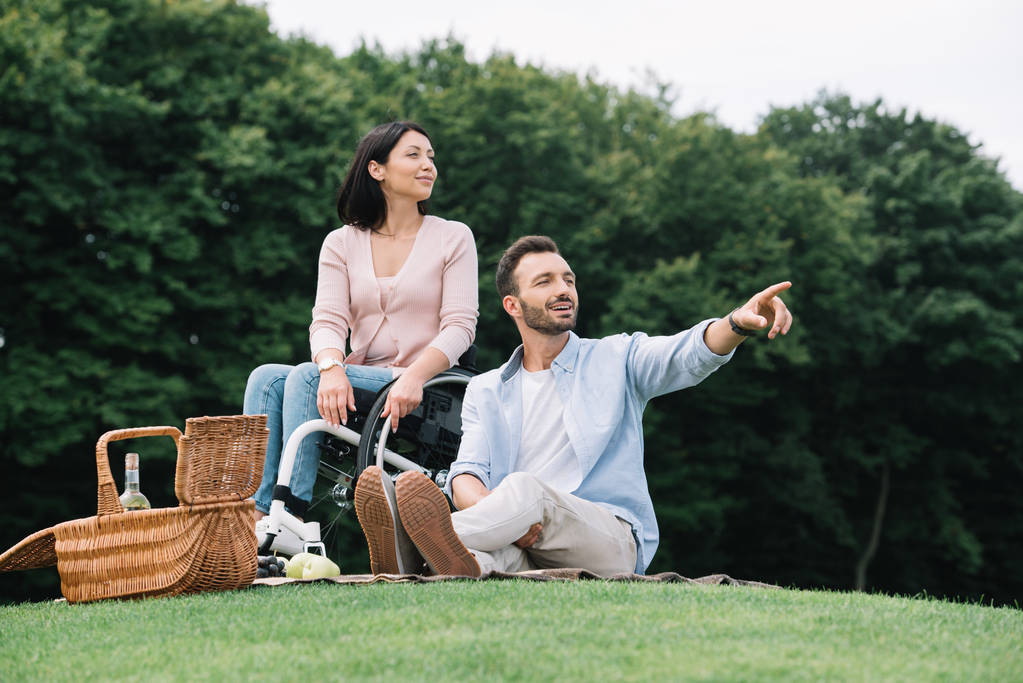 Красивый мужчина указывает пальцем, когда отдыхает в парке с девушкой-инвалидом
 - Фото, изображение