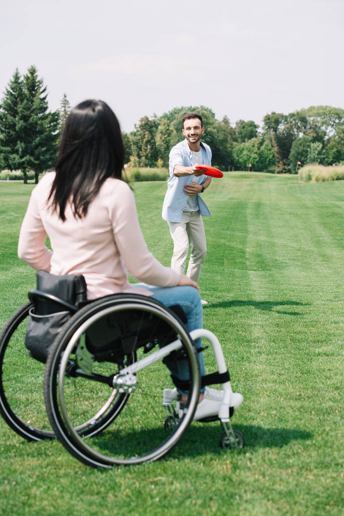 pohled na zdravotně postižené ženy hrající si na létající talíř s veselým přítelem v parku - Fotografie, Obrázek