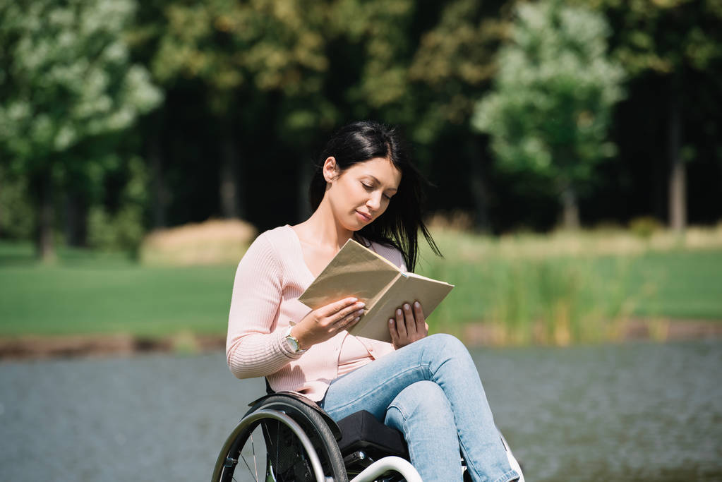 hermosa mujer discapacitada sonriendo mientras lee libro en el parque
 - Foto, imagen