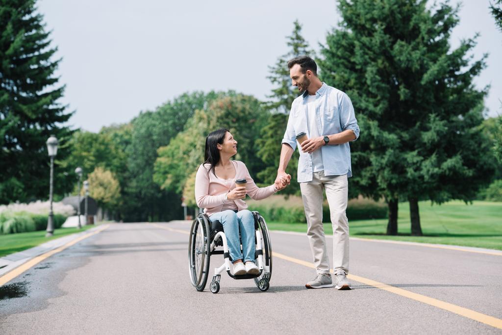 happy disabled woman holding hands with handsome boyfriend while walking in park together - Photo, Image