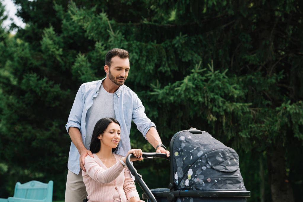 happy disabled woman and husband walking with baby carriage in park together - Photo, Image