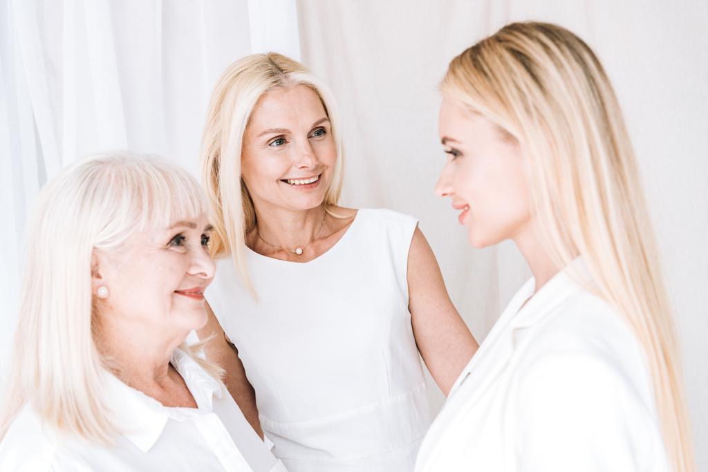κομψό τρεις-γενιά ξανθιές γυναίκες σε συνολικά λευκά ρούχα κοιτάζοντας ο ένας τον άλλο - Φωτογραφία, εικόνα