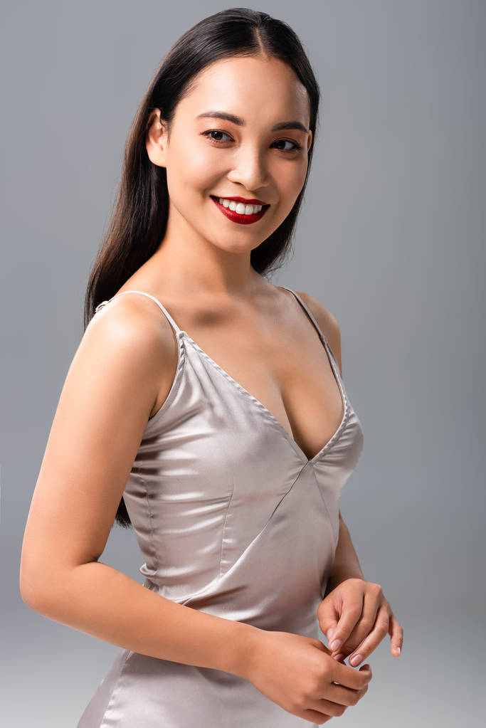 bela mulher asiática feliz em vestido de cetim com lábios vermelhos isolados em cinza
 - Foto, Imagem
