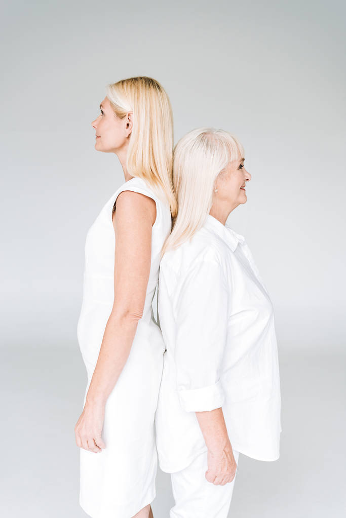 rubia madura hija y senior madre en total blanco trajes de pie espalda con espalda aislado en gris
 - Foto, Imagen