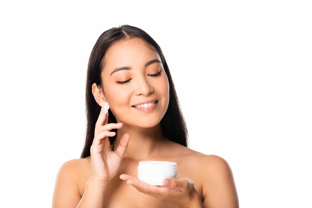 улыбающаяся обнаженная красивая азиатская женщина наносит косметический крем, изолированный на белом
 - Фото, изображение
