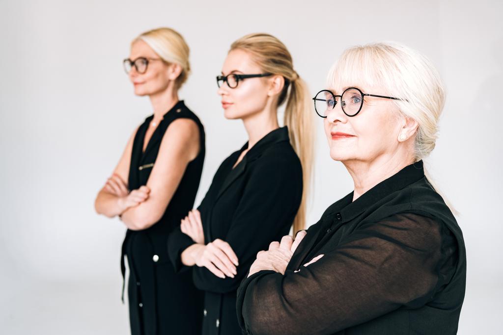 mulheres de negócios loira de três gerações na moda em roupas pretas totais e óculos com braços cruzados isolados em cinza
 - Foto, Imagem