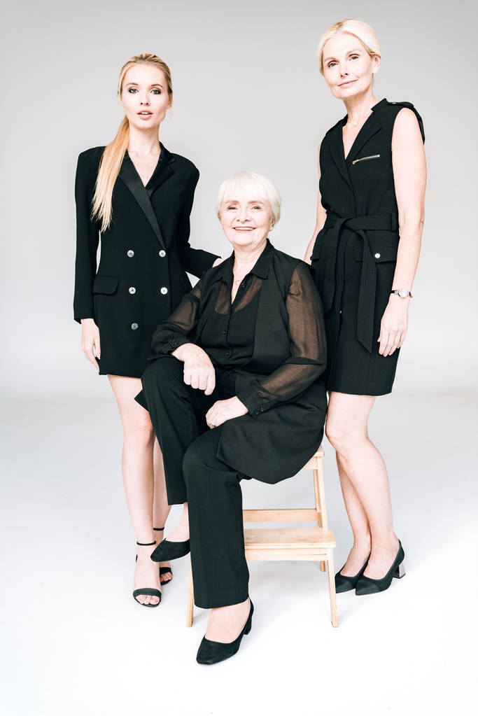 vista completa de elegantes mujeres rubias de tres generaciones en trajes negros totales aislados en gris
 - Foto, Imagen