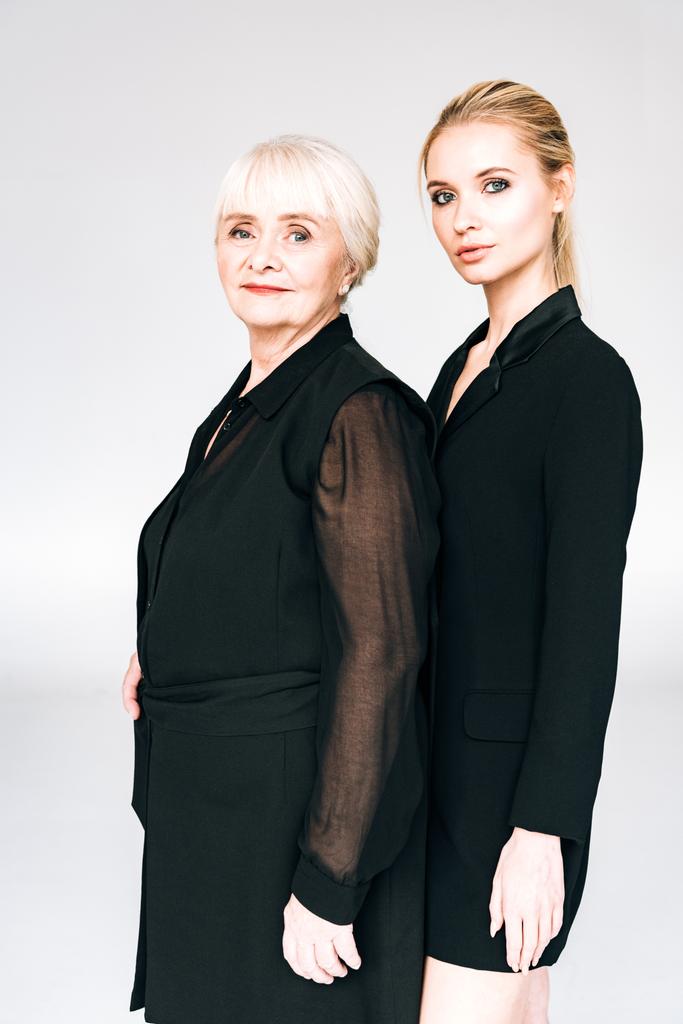 elegant blonde granddaughter and grandmother in total black outfits isolated on grey - Photo, Image