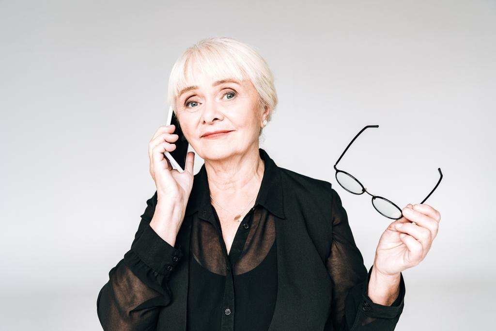 empresaria senior en traje negro con gafas hablando en smartphone aislado en gris
 - Foto, Imagen