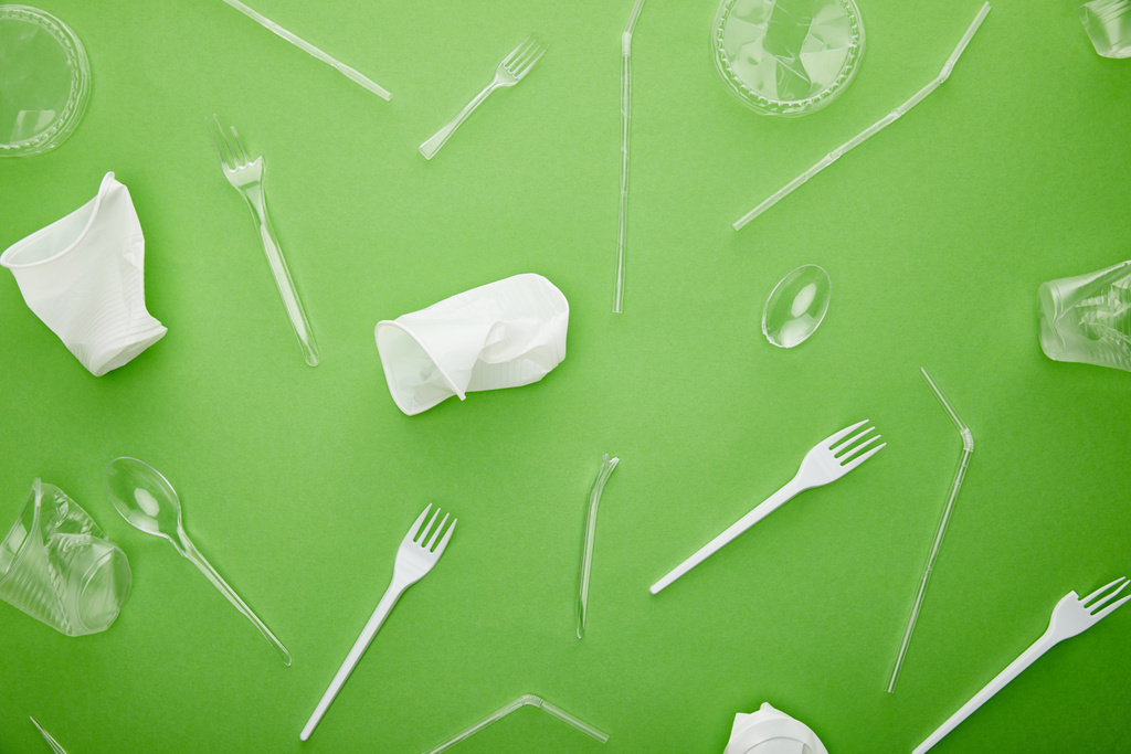 Top zicht op wegwerp plastic bekers, vorken en lepels op groene achtergrond - Foto, afbeelding