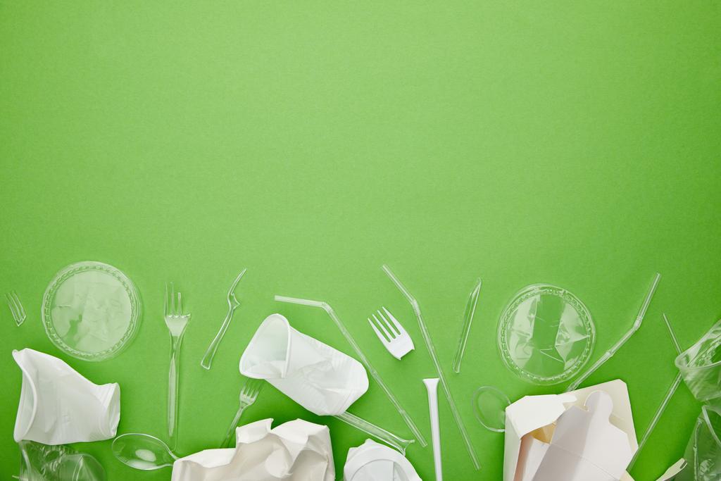 Κορυφαία όψη των πλαστικών κυπελλών μίας χρήσης, πιρούνια, κουτάλια και δοχεία από χαρτόνι σε πράσινο φόντο με χώρο αντιγραφής - Φωτογραφία, εικόνα