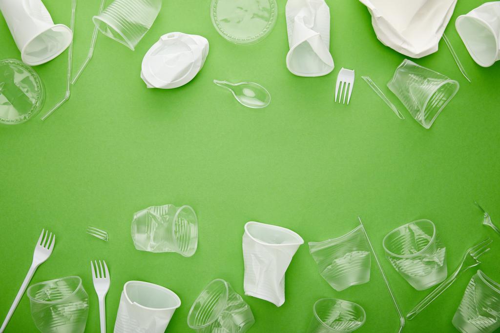Draufsicht auf zerknüllte Plastikbecher, Gabeln und Teller auf grünem Hintergrund mit Kopierraum  - Foto, Bild