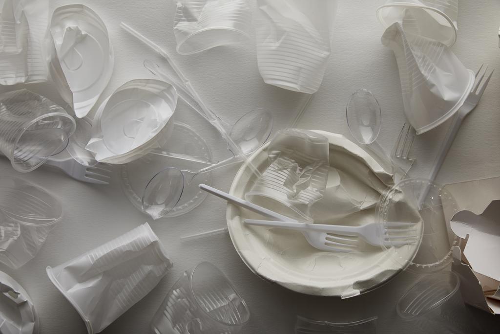 Κορυφαία όψη των τσαλακωμένες πλάκες μίας χρήσης, πλαστικά κύπελλα, πιρούνια και κουτάλια σε λευκό φόντο  - Φωτογραφία, εικόνα