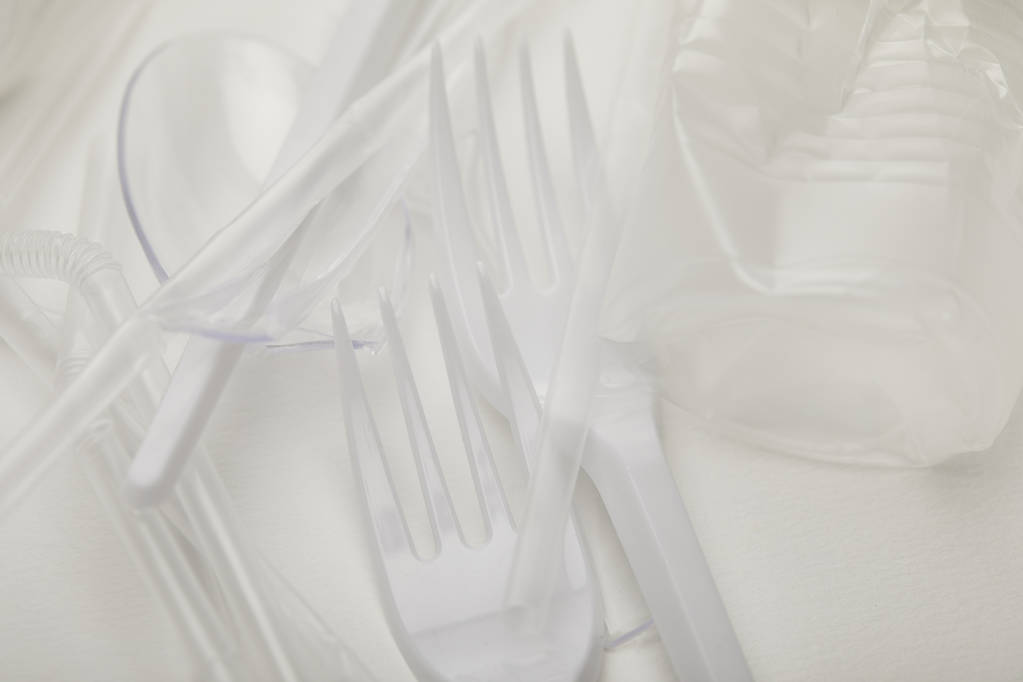 lähikuva rypistyneestä muovikupista, haarukoista ja lusikoista valkoisella pohjalla
 - Valokuva, kuva