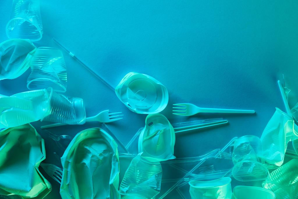 az gyűrött műanyag csészék, szalmák és a villák felülnézete a kék fényben található másolási hellyel - Fotó, kép