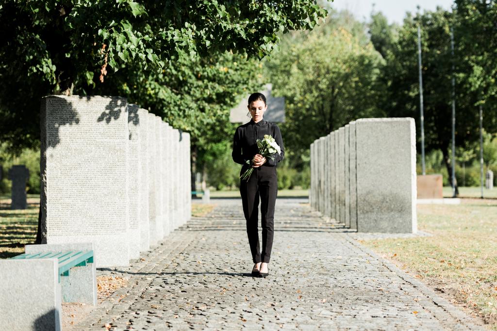 rozrušená žena držící květiny a procházky na hřbitově  - Fotografie, Obrázek