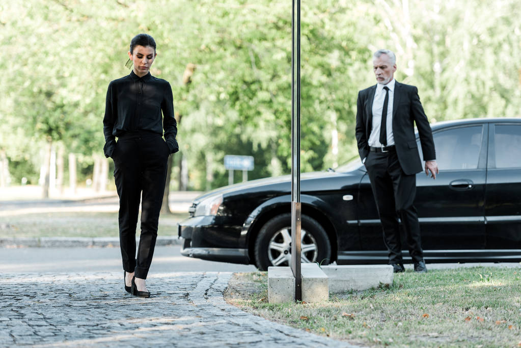黒い車の近くを歩くフォーマルな服装で動揺した男女  - 写真・画像