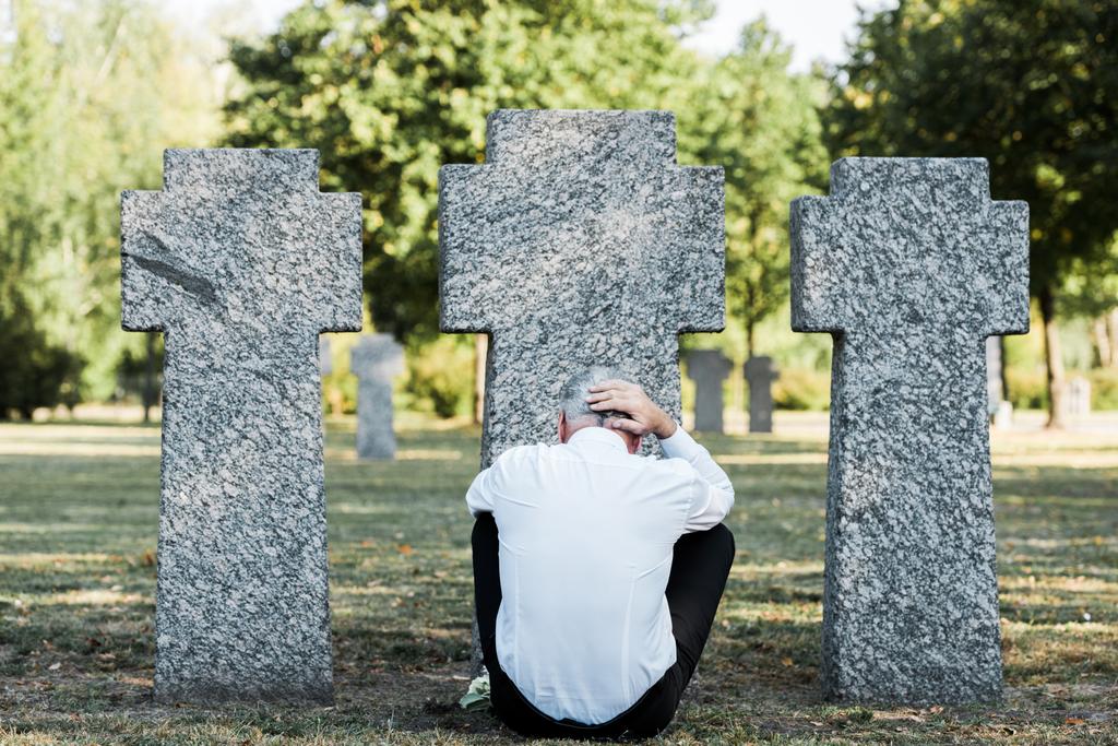 Achteraanzicht van de mens met grijs haar zittend in de buurt van grafstenen  - Foto, afbeelding