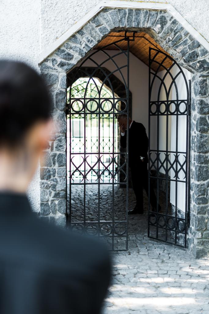 επιλεκτική εστίαση του θλιβερά ανώτερου άντρα που στέκεται στο κτίριο κοντά σε γυναίκα στο νεκροταφείο  - Φωτογραφία, εικόνα