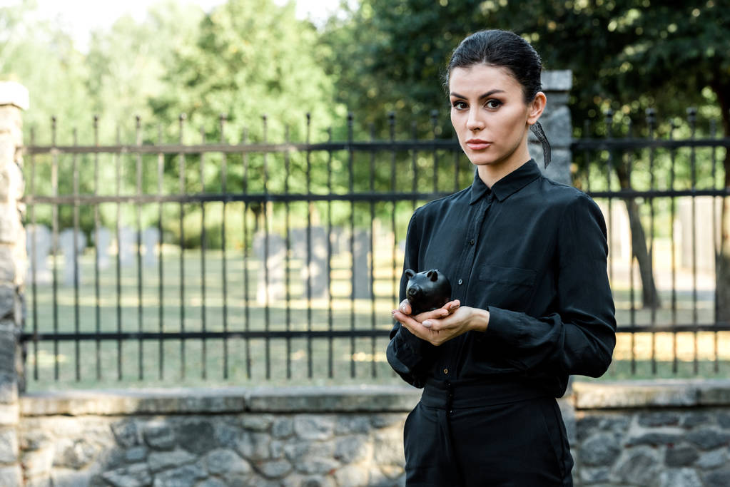 atrakcyjny kobieta trzyma czarny Skarbonka w pobliżu metalowe ogrodzenia  - Zdjęcie, obraz