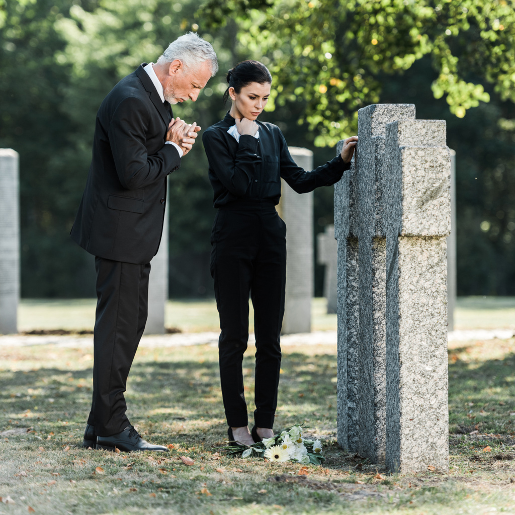 αναστατωμένος άνθρωπος με γκρίζα μαλλιά και ελκυστική γυναίκα στέκεται κοντά στους τάφους  - Φωτογραφία, εικόνα