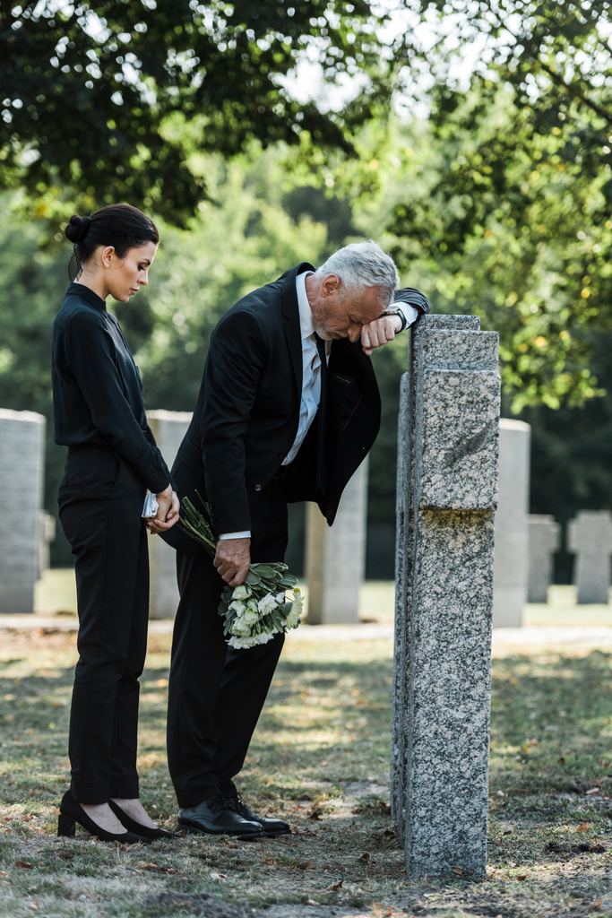 привлекательная женщина с цветами возле надгробий и расстроенный пожилой мужчина
  - Фото, изображение