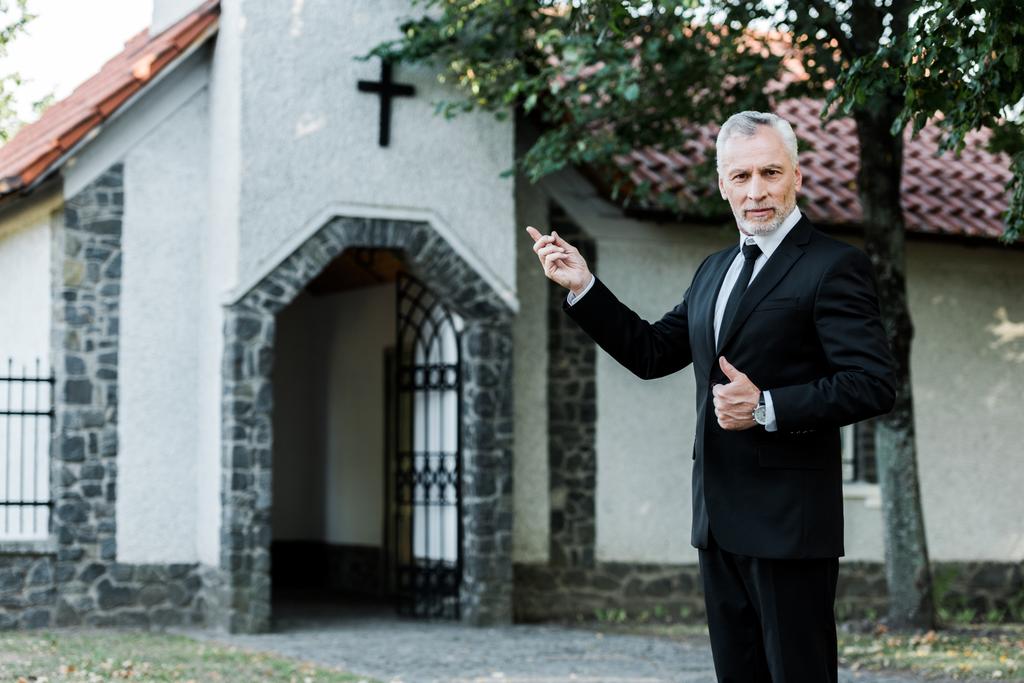Senior zeigt Daumen hoch und zeigt mit Finger auf Kirche  - Foto, Bild