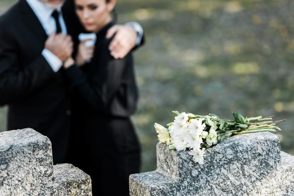 selective focus of flowers on tomb near senior man hugging woman  - Photo, Image