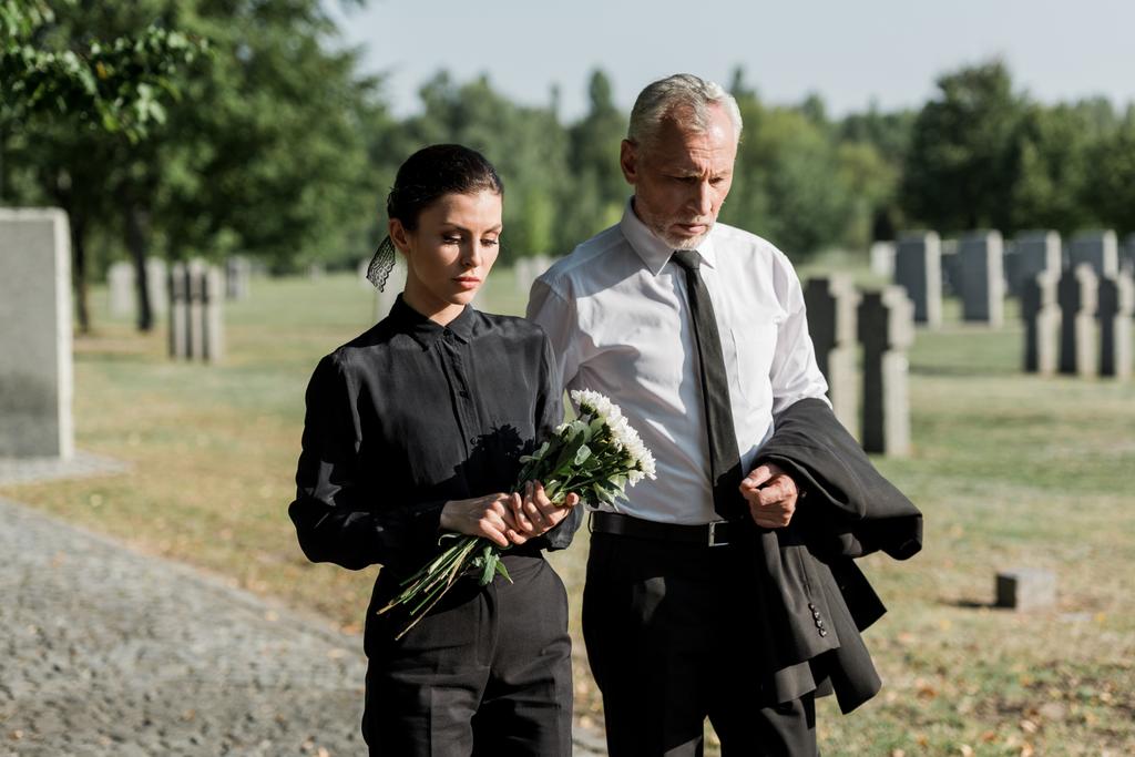 γένια ανώτερος άνθρωπος περπάτημα κοντά σε γυναίκα με λουλούδια στην κηδεία - Φωτογραφία, εικόνα