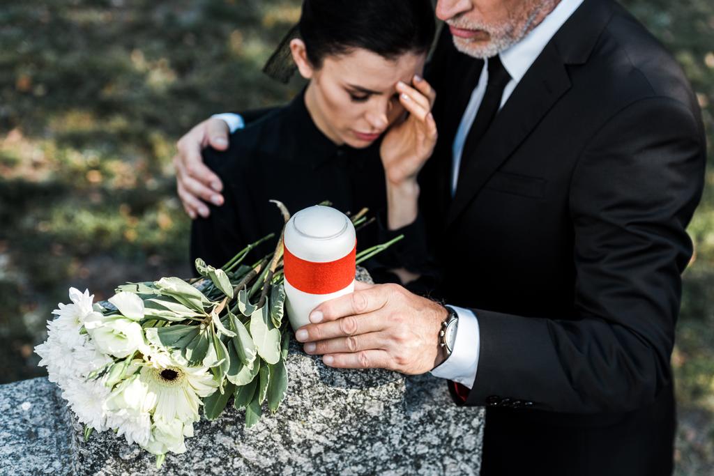 szelektív középpontjában a virágok sír közelében vezető ember ölelve ideges nő  - Fotó, kép
