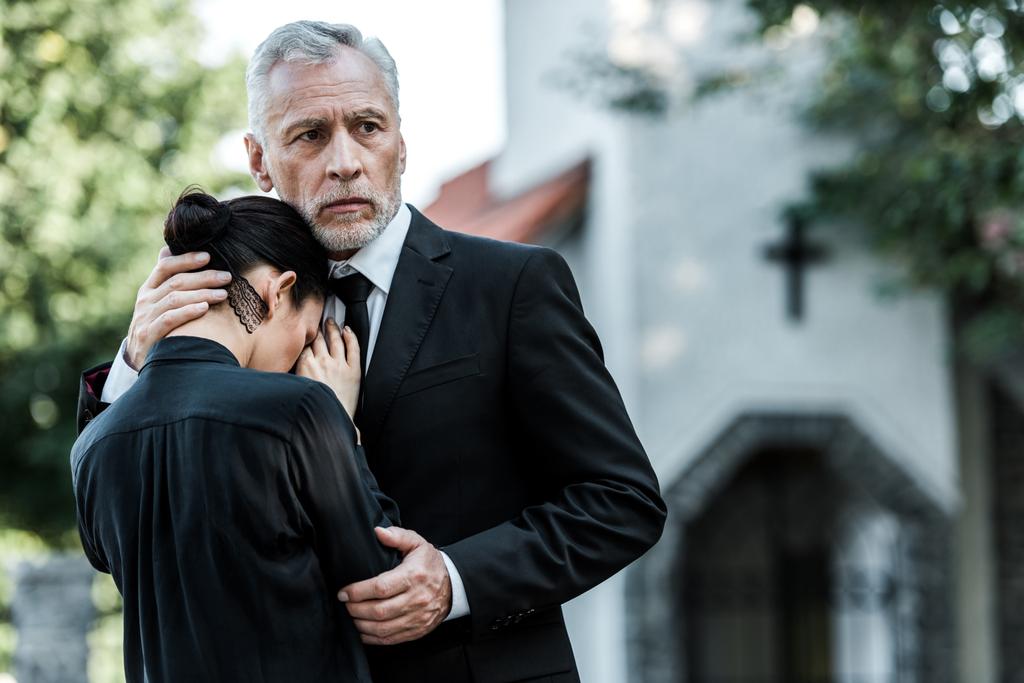 грустный мужчина обнимает расстроенную женщину возле церкви
  - Фото, изображение