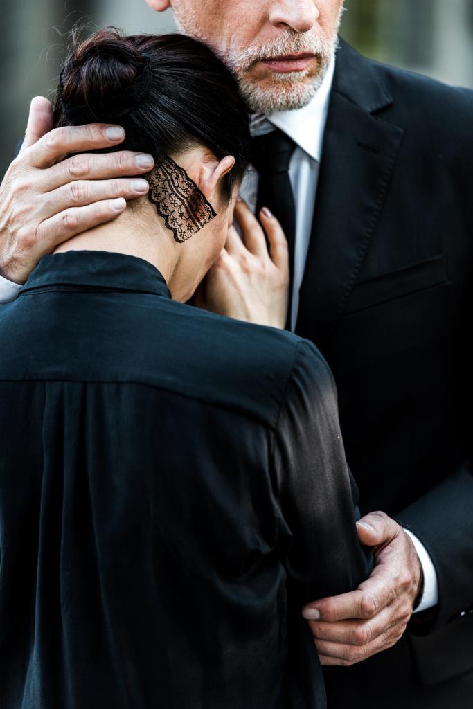 обрезанный вид пожилого бородатого мужчины, обнимающего женщину на похоронах
  - Фото, изображение
